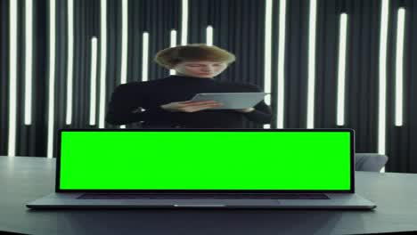 mujer trabajando en una tableta, portátil con pantalla verde en una oficina moderna