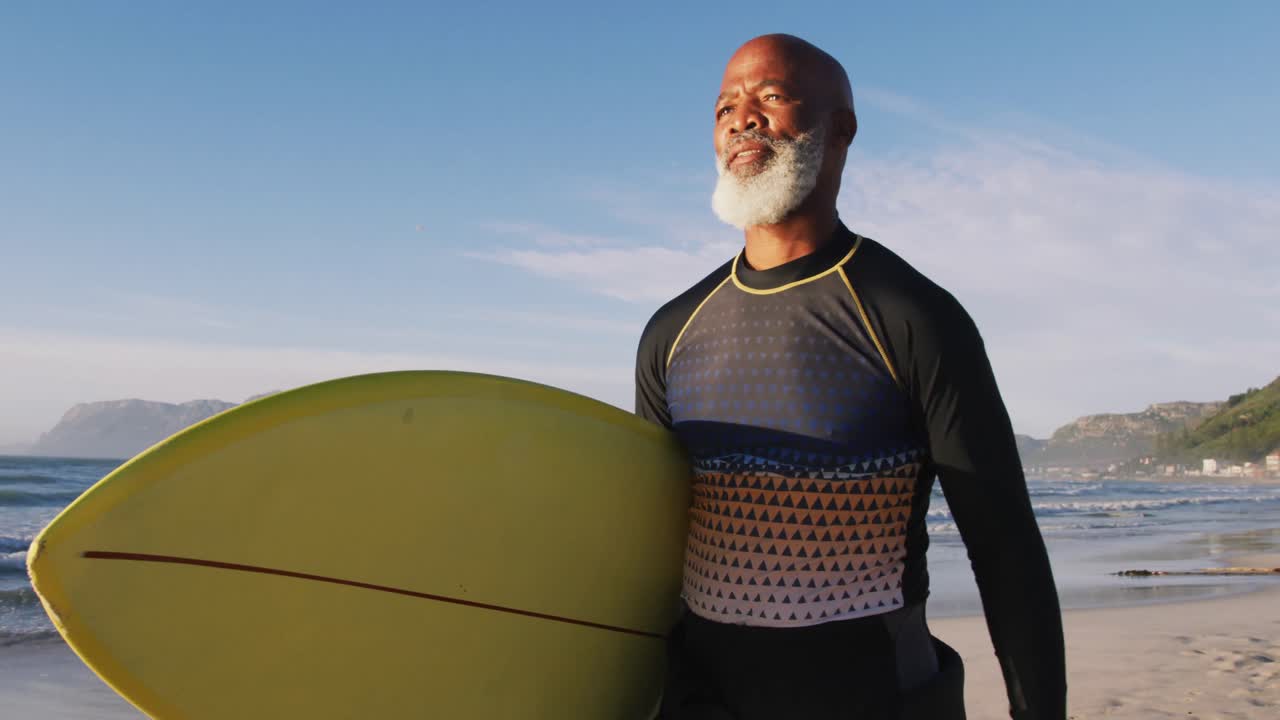 Senior african american man walking with a surfboard at the beach