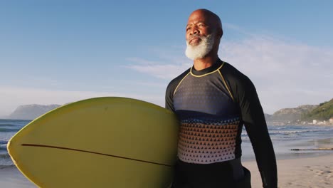 Älterer-Afroamerikanischer-Mann,-Der-Mit-Einem-Surfbrett-Am-Strand-Spaziert