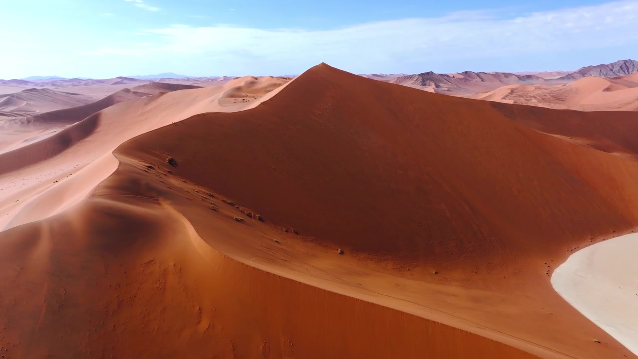 Vista de drone de uma única duna de areia vermelha imponente com cristas afiadas no campo de dunas de Sossusvlei. As imponentes dunas vermelhas brilham contra as planícies de argila pálida e rachada desta antiga área selvagem desértica.