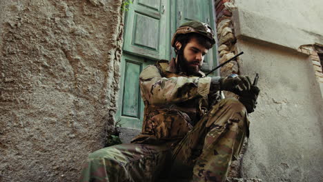 soldier sitting near a destroyed house checks his compass