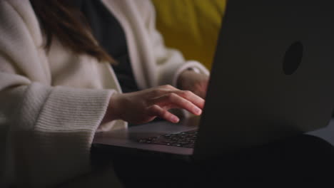 close up of woman typing on laptop keyboard spending evening at home sitting on sofa browsing online