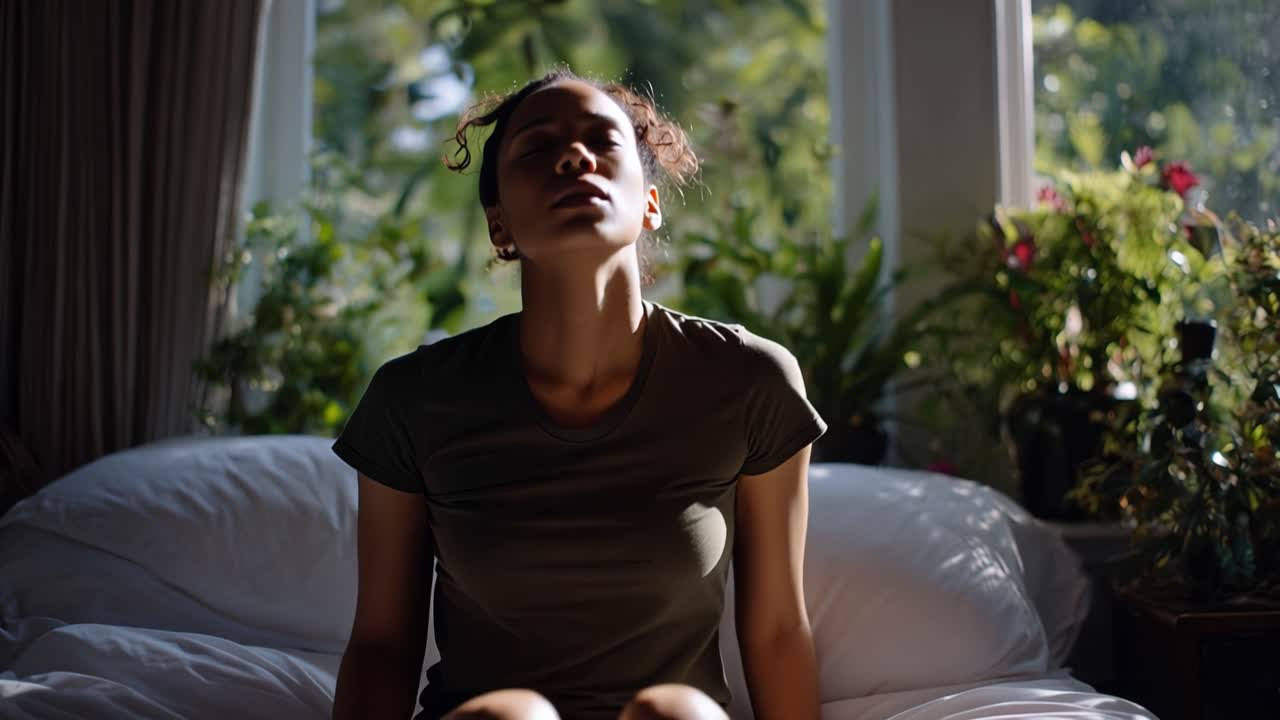 Une douce lumière du soleil baigne une femme fatiguée. Elle se tient les tempes, les yeux fermés. Sa tête est penchée en arrière, les mains appuyées sur la nuque. Elle est assise, les yeux baissés, respirant lentement. Stress, fatigue, ou contemplation paisible.