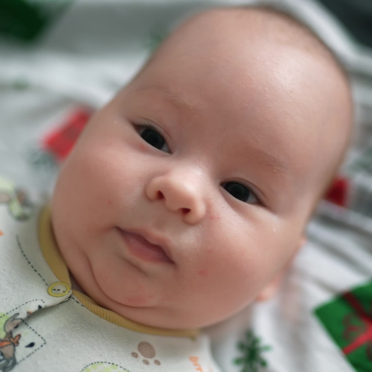 Small infant boy with plump cheeks resting on the bed. Beautiful toddler watching intensely the camera. Top view close up