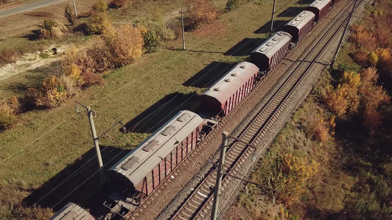 freight train with wagons is passing by rail near landings with trees on the background of fields in warm weather. Aerial view