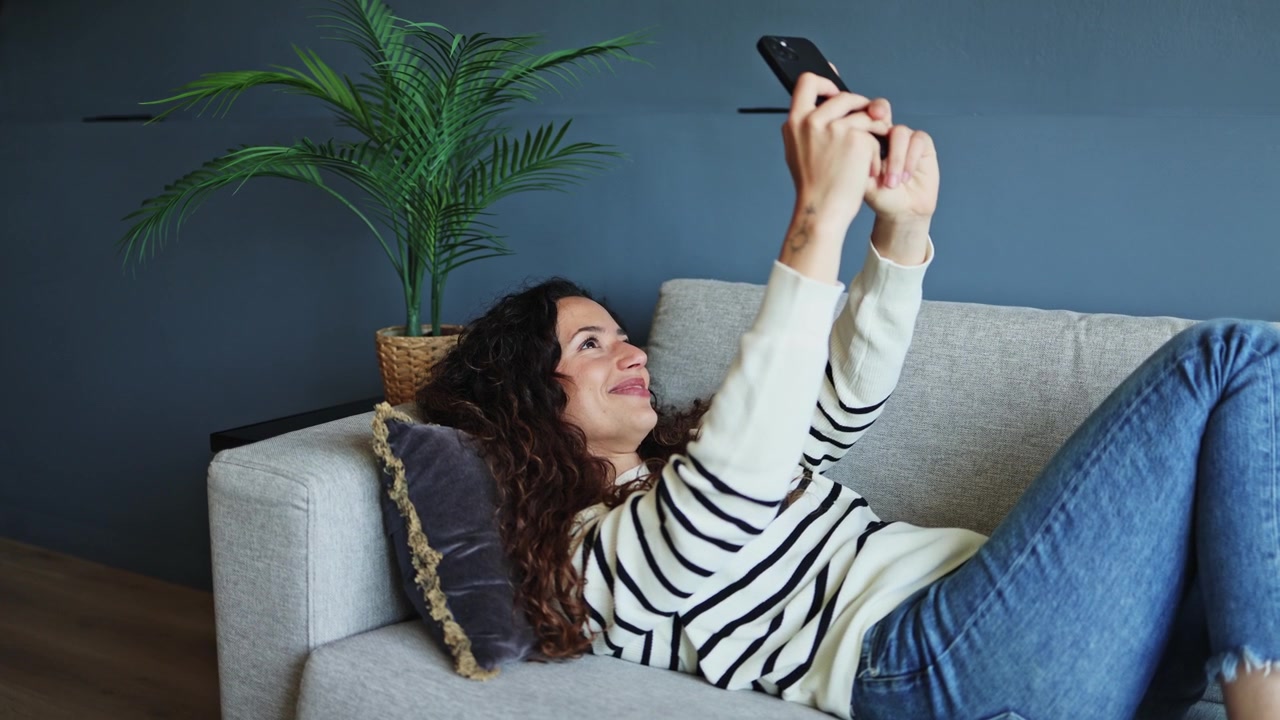 Giovane donna che si rilassa sul divano e usa lo smartphone