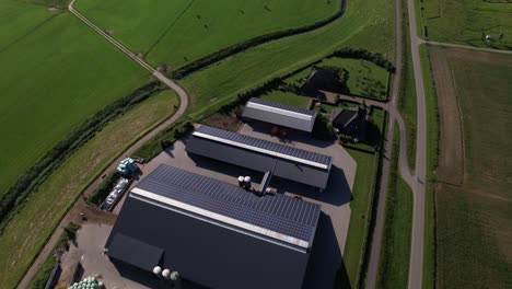 Aerial-view-of-large-farm-with-solar-panels-in-Dutch-river-valley-landscape-following-the-embankment-with-a-road-on-top-meandering-through-the-agrarian-rural-area-near-Zutphen,-Netherlands