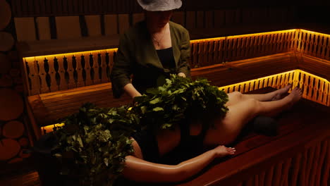 woman receiving a banya treatment in a wooden sauna
