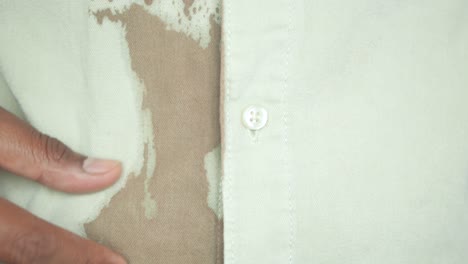 close-up of a man pointing at a brown stain on a white shirt