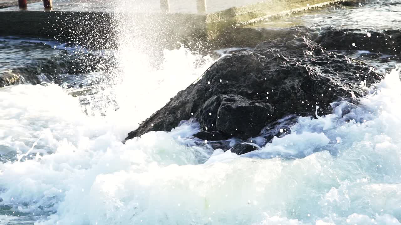 Sea waves hit the rocks and fly around with a lot of splashes. Big wave crashing into the big rock and becomes the white foam. Awesome power of waves breaking over dangerous rocks