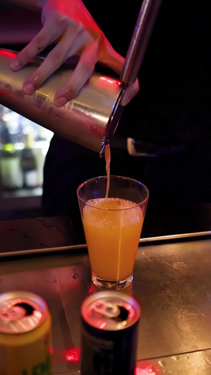 Un barista versa un cocktail vivace sul ghiaccio in un bar di Bangkok in penombra, primo piano, telecamera fissa