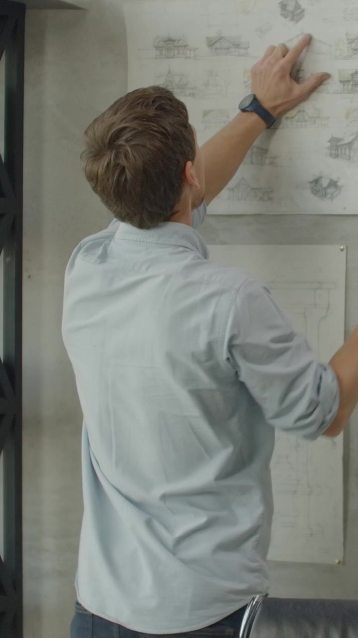 Architect Reviewing and Hanging Blueprints in Modern Office
