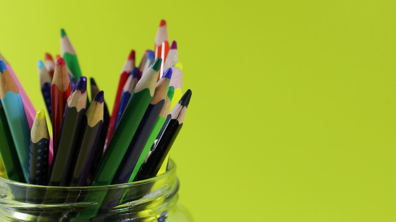 lápiz de colores en frasco de vidrio girando sobre fondo amarillo con espacio de copia. bucle sin costuras