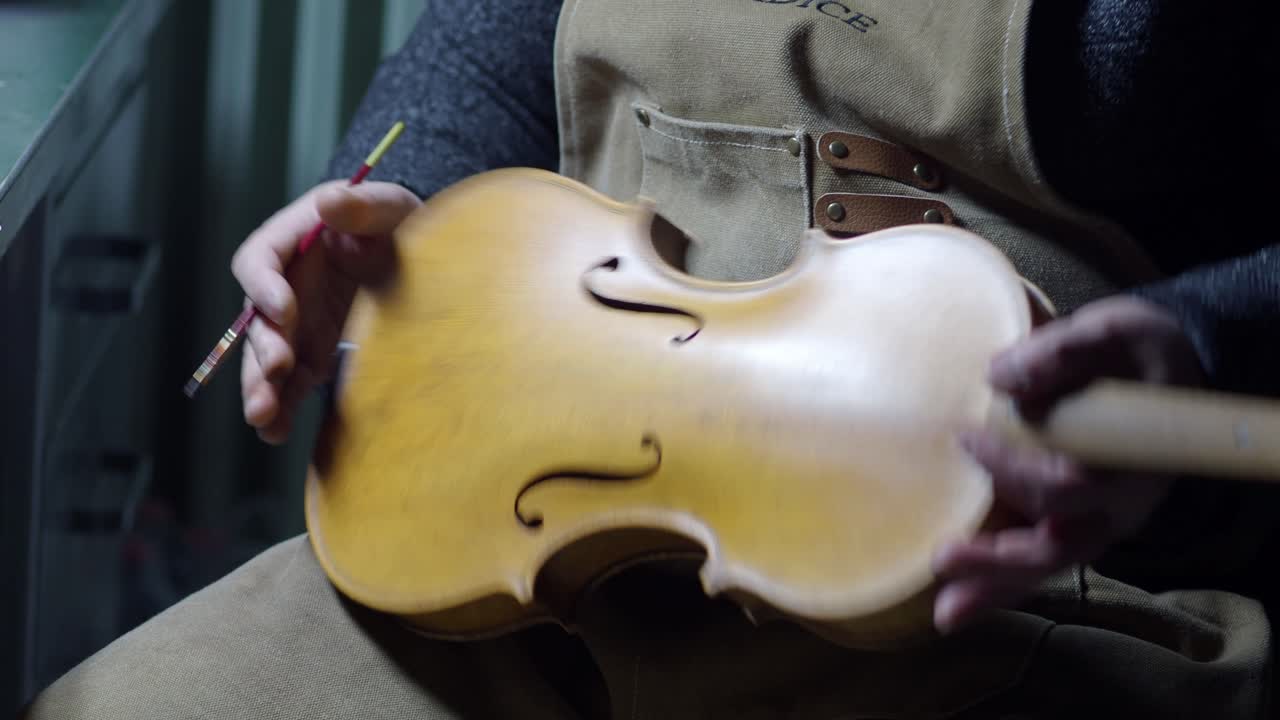 Master craftsman meticulously applies protective varnish to an aged wooden violin body showcasing intricate details and traditional woodworking techniques