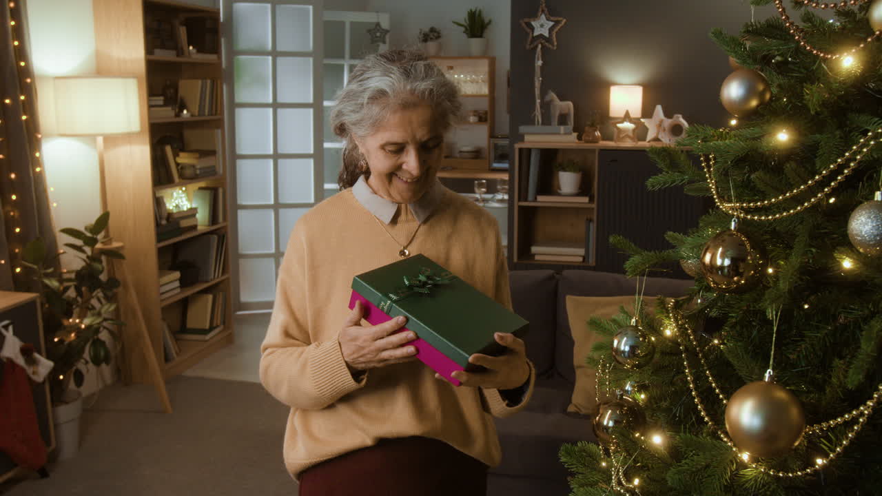 Elderly Woman Holding a Christmas Gift Next to a Christmas Tree