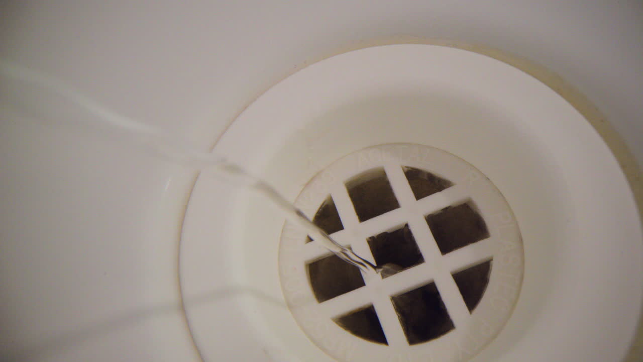 water vortex shot macro extrema subacuática de cerca de un orificio del tapón de la bañera mientras el agua del baño se vacía con un suave y delgado vórtice sobre el orificio