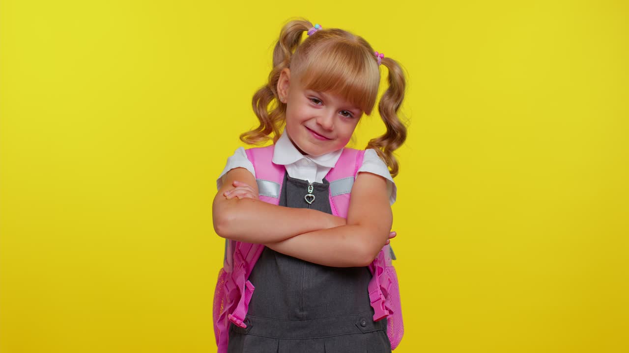 una atractiva estudiante rubia adolescente con uniforme escolar lleva una mochila rosa con los brazos cruzados