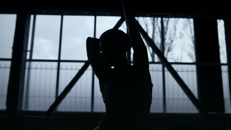 flexible dancer silhouette moving hands in dark gym. slim woman dancing indoors.