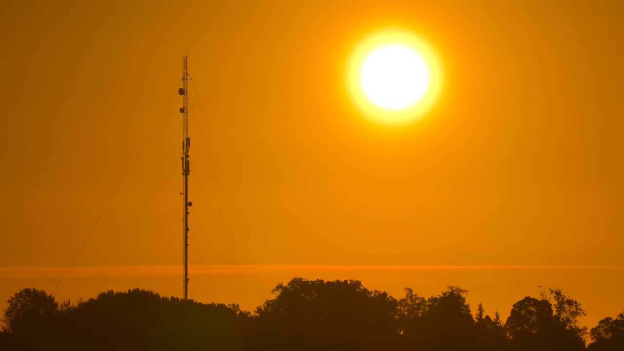 Static shot of deep yellow sunrise sky and round sun near tower, Latvia