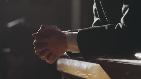 cinematic tracking priest's hands clasped in prayer.