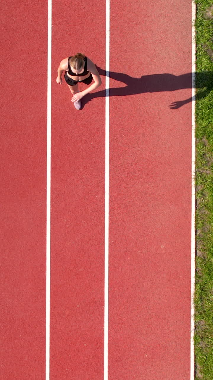 A vertical aerial shot of a female athlete sprinting on a stadium running track during a sunny day. Ideal for fitness, sports, and healthy lifestyle content