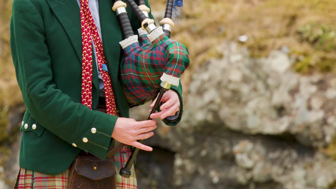 Man in kilt plays bagpipes outdoors, natural daylight, medium shot, traditional Scottish dress