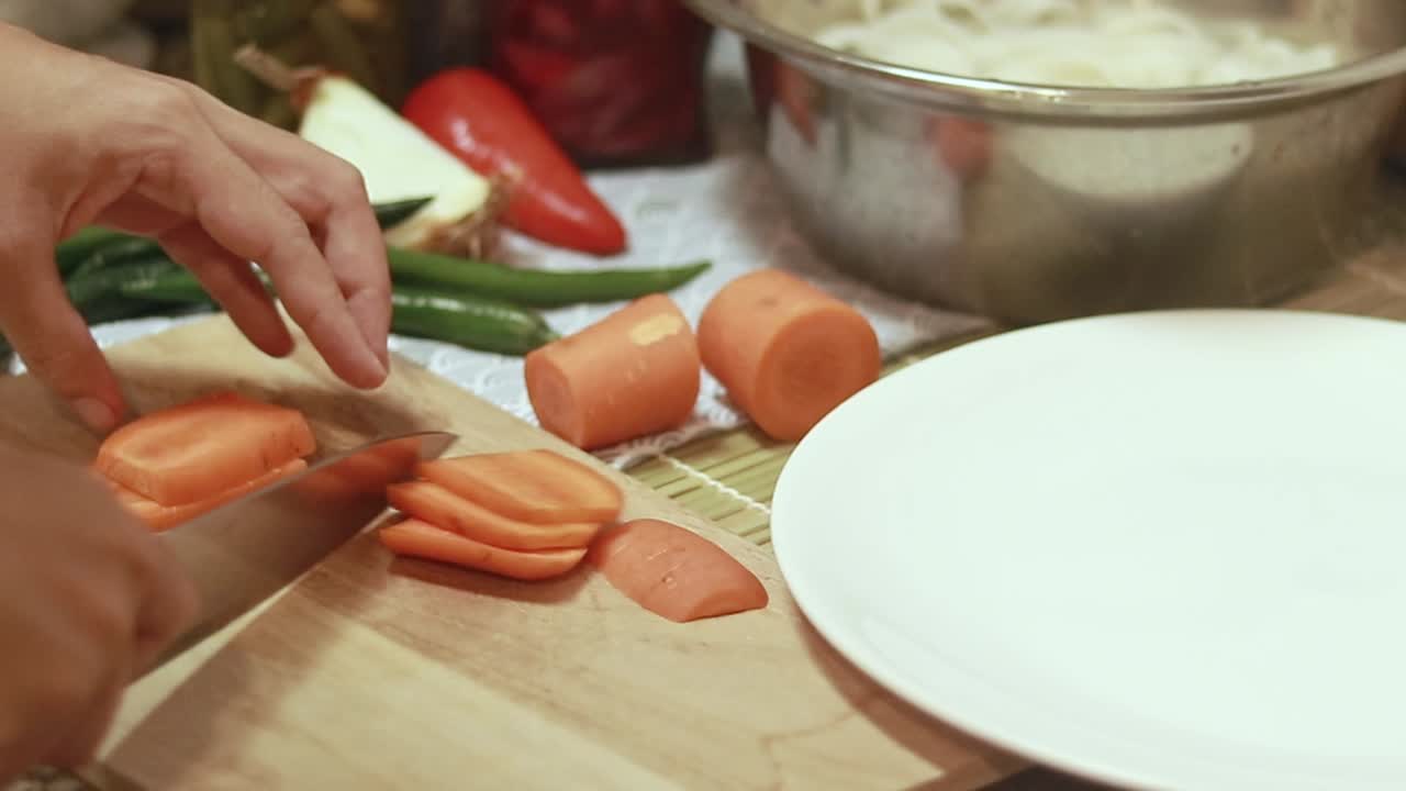 Close-up of hands slicing carrots on a wooden cutting board in a kitchen setting showing candid domestic daily life