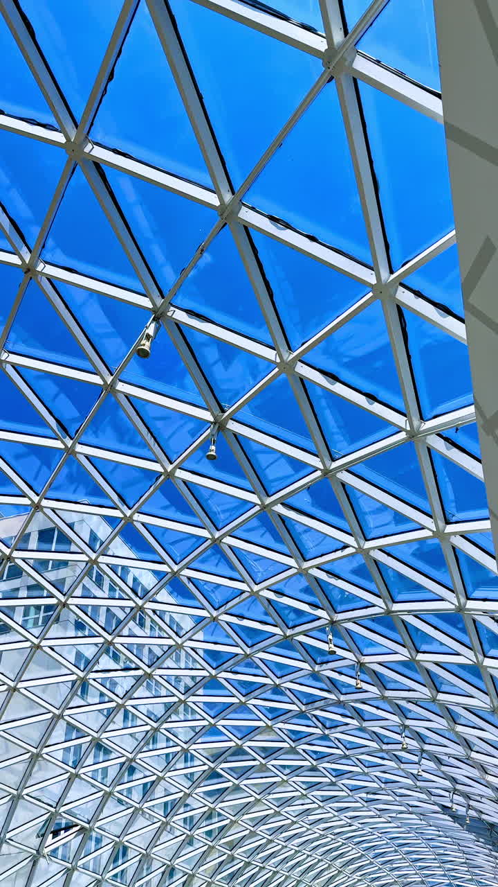 Metal constructions and lamps on the glass ceiling. Blue sky is seen through the roof. Vertical video.