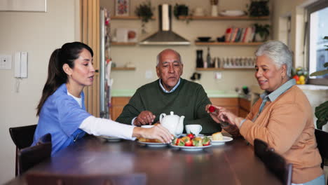 a nurse and two elderly patients sit at a table enjoying a meal