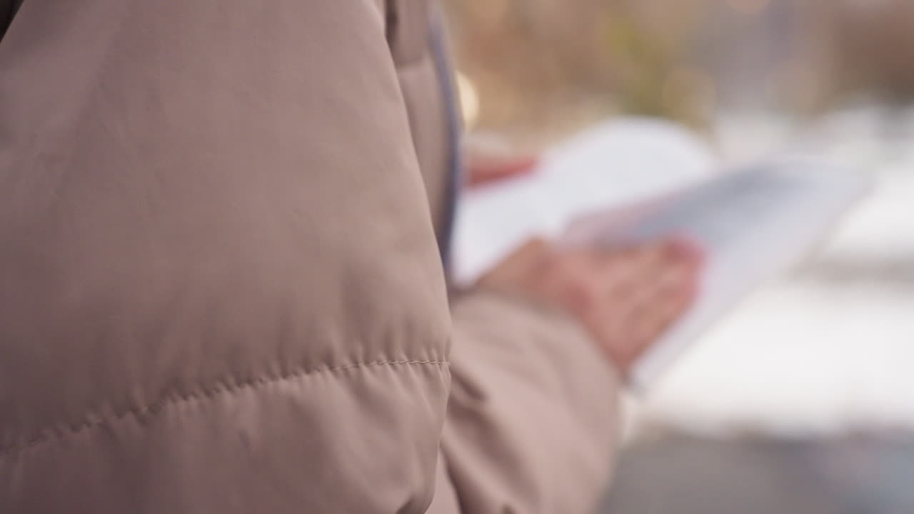 Side view of individual wearing autumn coat holding open book outdoors, blurred text and background create soft focus effect, capturing peaceful moment of reading in cold weather