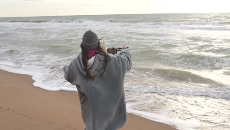 woman recording video on beach at sunset/sunrise