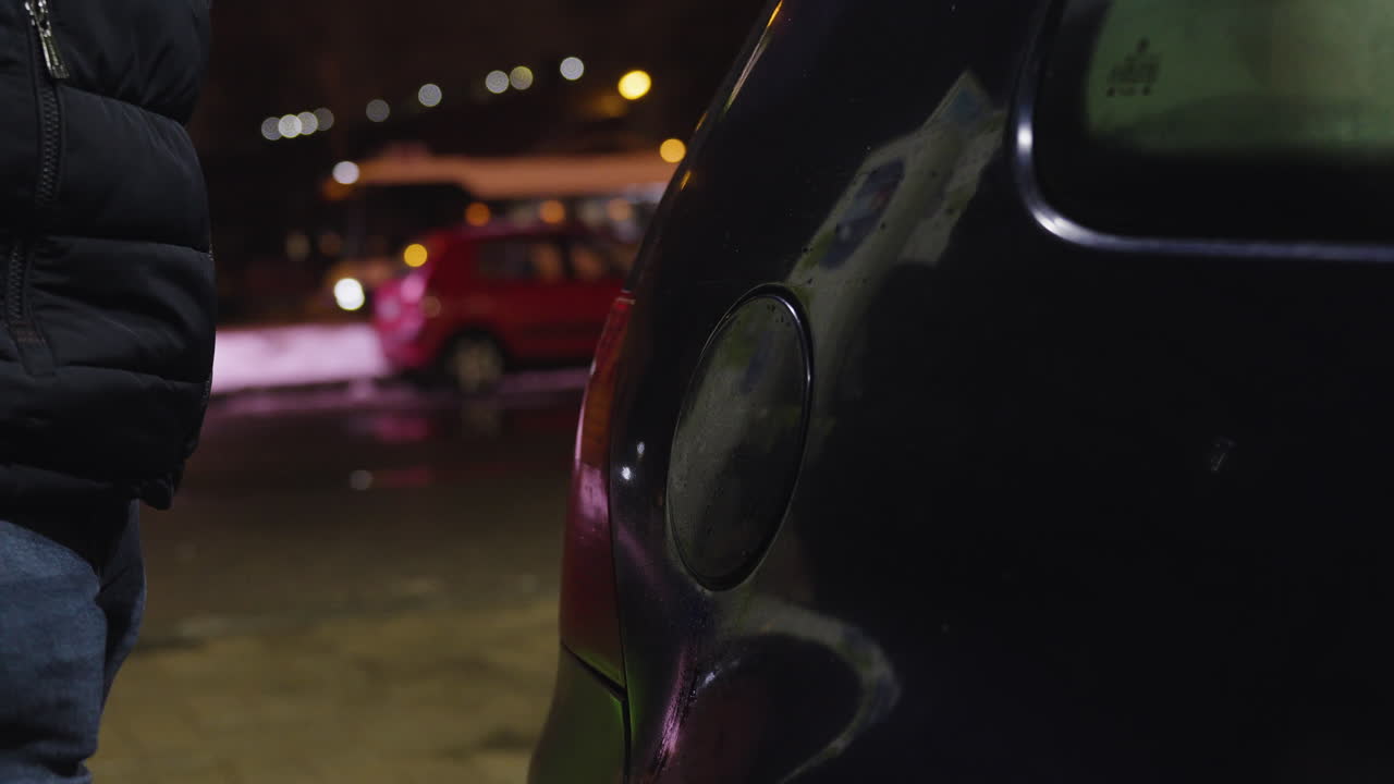 Vista laterale di un uomo che apre il tappo del serbatoio dell'auto per fare benzina in una notte fredda.
