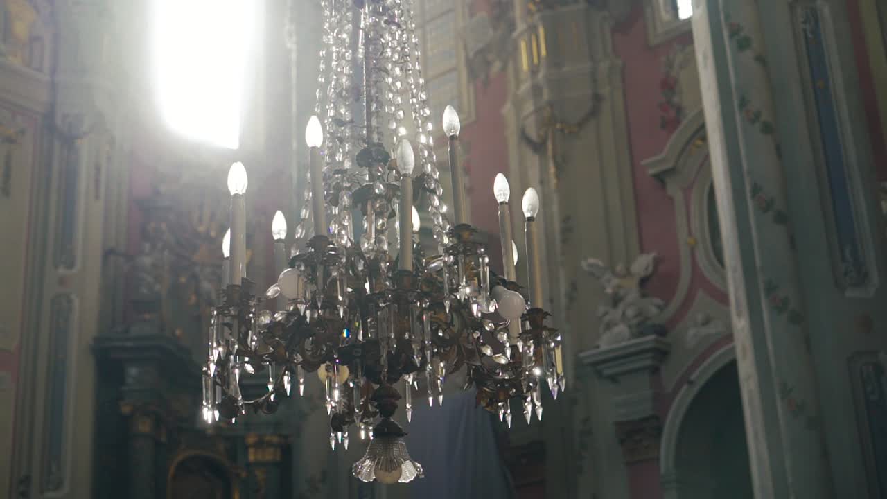 a luxurious chandelier hangs in the middle of a catholic cathedral on the background of frescoes. Camera motion to the side