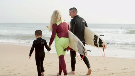 happy family of surfers walking on seacoast