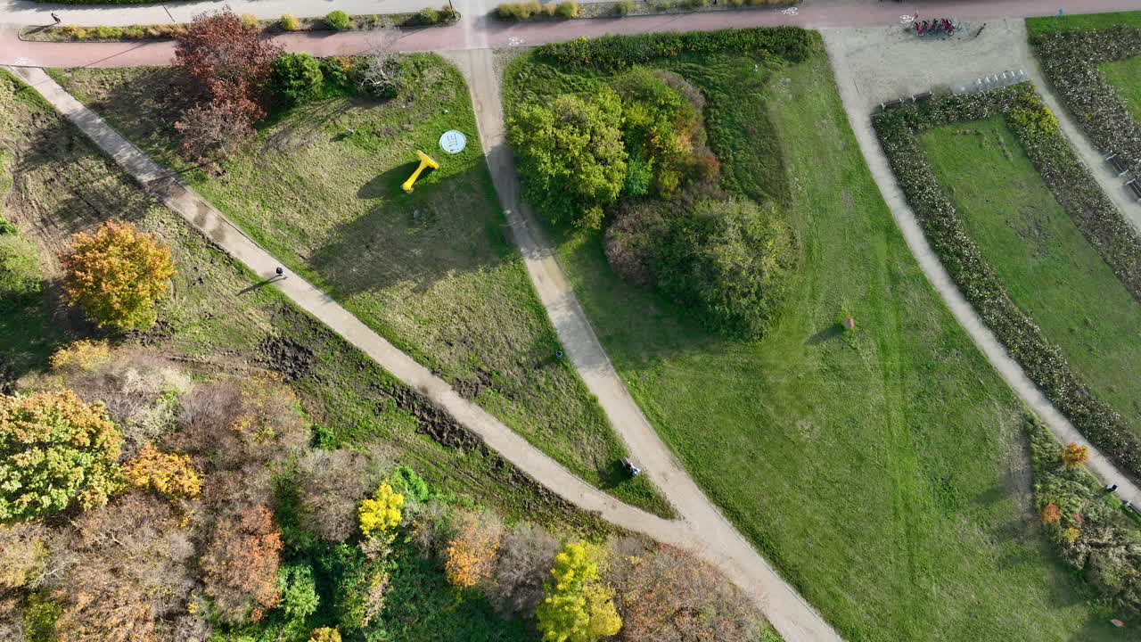 Top-down drone shot of walking paths, grassy areas and outdoor sculptures in a landscaped park