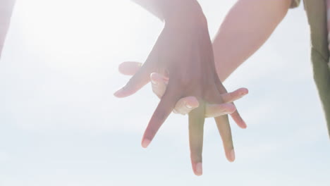 midsection of diverse female gay couple holding hands walking along beach