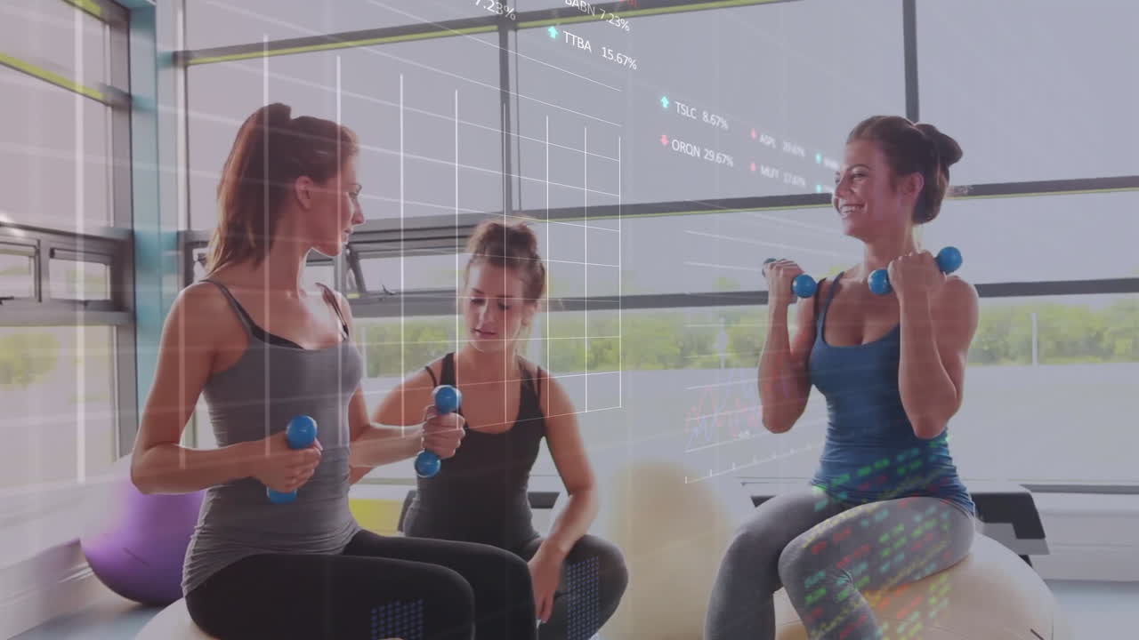 Three women pumping dumbbells on stability balls in fitness studio, with digital graphs floating
