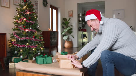 senior man wrapping christmas gifts at home near decorated tree, smiling warmly