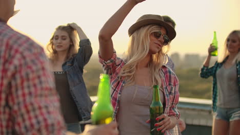 a young blonde in glasses and a hat moves in a dance with her friends on the roof. they celebrate a rooftop party