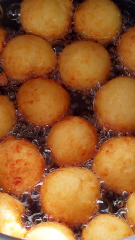 lots of donuts with no hole in the middle are fried in oil deep. close up view on the sweet dough pastry cooking. vertical video.