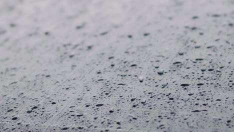 close up footage of raindrops slowly rolling down a dark car window during a downpour