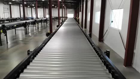 a conveyor belt system stretches through a spacious warehouse, smoothly transporting items along its length. workers are seen managing the process as daylight fills the space.