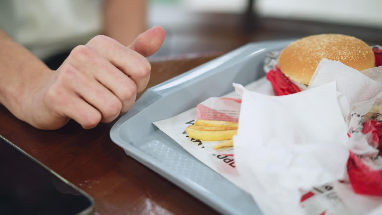 Primo piano di un vassoio bianco pieno di hamburger e patatine fritte, con polpetta succosa e patate croccanti visibili, condimenti lucidi, in un ambiente da pasto informale, con attenzione alla consistenza e al colore, molto appetitoso.