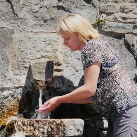 a tired woman washes takes water from an old faucet in a stone wall 1