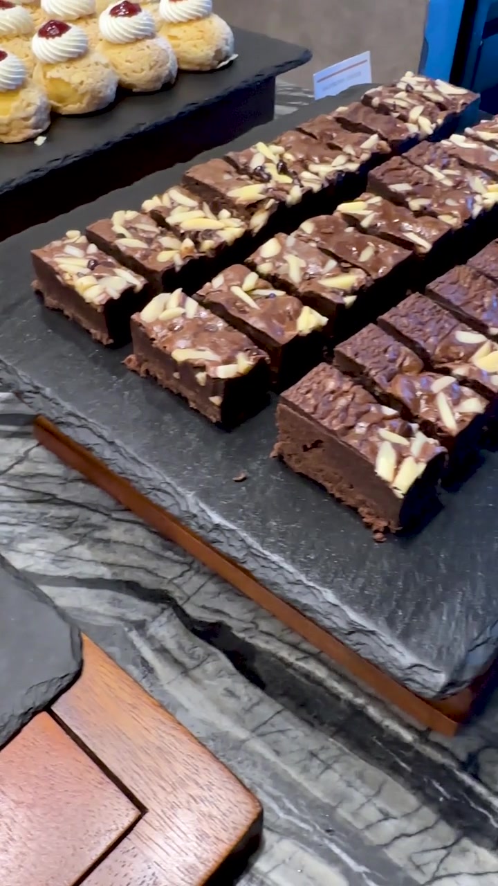 A camera pans across rows of strawberry shortcakes, caramel squares, and chocolate brownies on slate