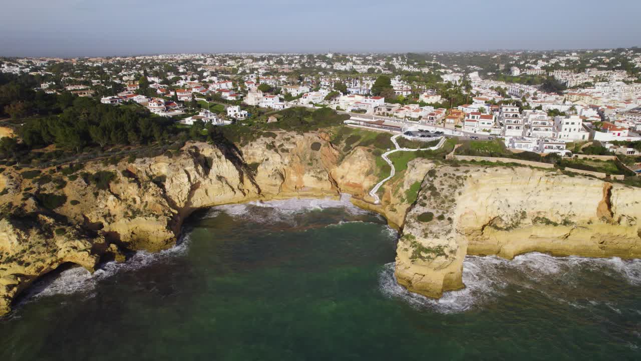 las olas chocan contra los acantilados y la ciudad marítima de carvoeiro en portugal, aérea