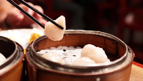 chopsticks picking dumplings from a bamboo steamer