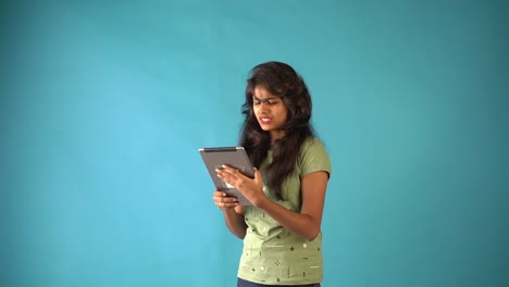 A-young-Indian-girl-in-green-t-shirt-talking-in-video-chat-in-tab-standing-in-an-isolated-blue-background-studio