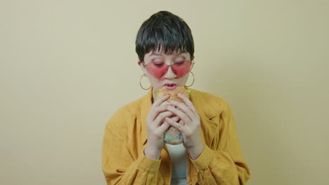 short-haired alternative woman eating a hamburger and nodding with pleasure as she savors it