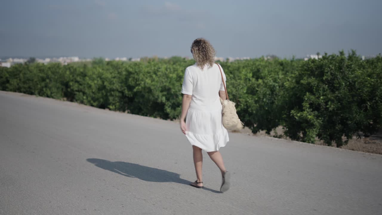 Woman Walking on a Road Through a Fruit Orchard